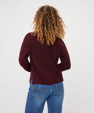 Woman wearing a burgundy V-neck sweater with long sleeves and a relaxed fit, paired with wide-leg blue jeans.
