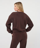 Back view of a woman wearing the Sloane Side-Tie Sweater in chocolate brown, showing the relaxed silhouette, long sleeves, and clean back design.