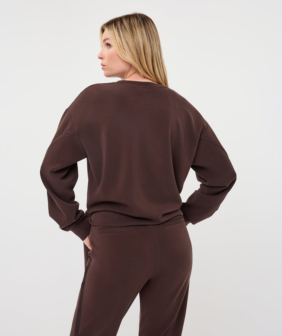 Back view of a woman wearing the Sloane Side-Tie Sweater in chocolate brown, showing the relaxed silhouette, long sleeves, and clean back design.