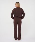 Full-length back view of a woman wearing the chocolate brown Sloane Side-Tie Sweater with matching relaxed-fit trousers, highlighting the coordinated look and fluid drape.