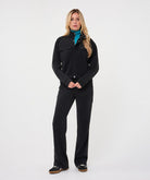 Woman wearing a black utility jacket with a stand collar and flap chest pockets over a turquoise knit top, paired with matching trousers.