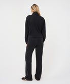 Woman wearing a black utility jacket with a stand collar paired with matching trousers seen from the back.