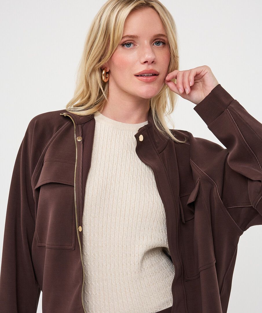 Woman wearing a chocolate brown utility jacket over a cream ribbed knit sweater