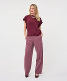 Woman wearing a burgundy satin roll-sleeve top with mauve pinstripe wide-leg trousers, front view.