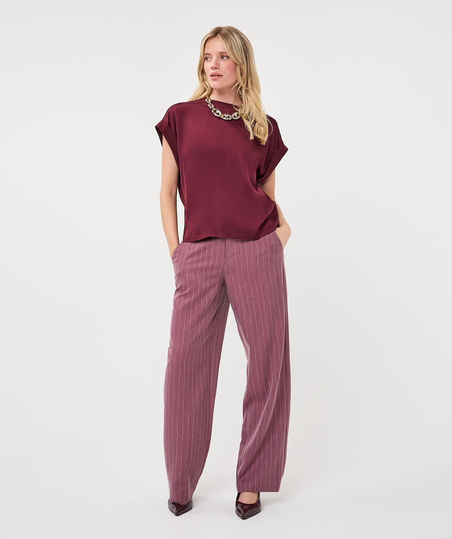 Woman wearing a burgundy satin roll-sleeve top with mauve pinstripe wide-leg trousers, front view.