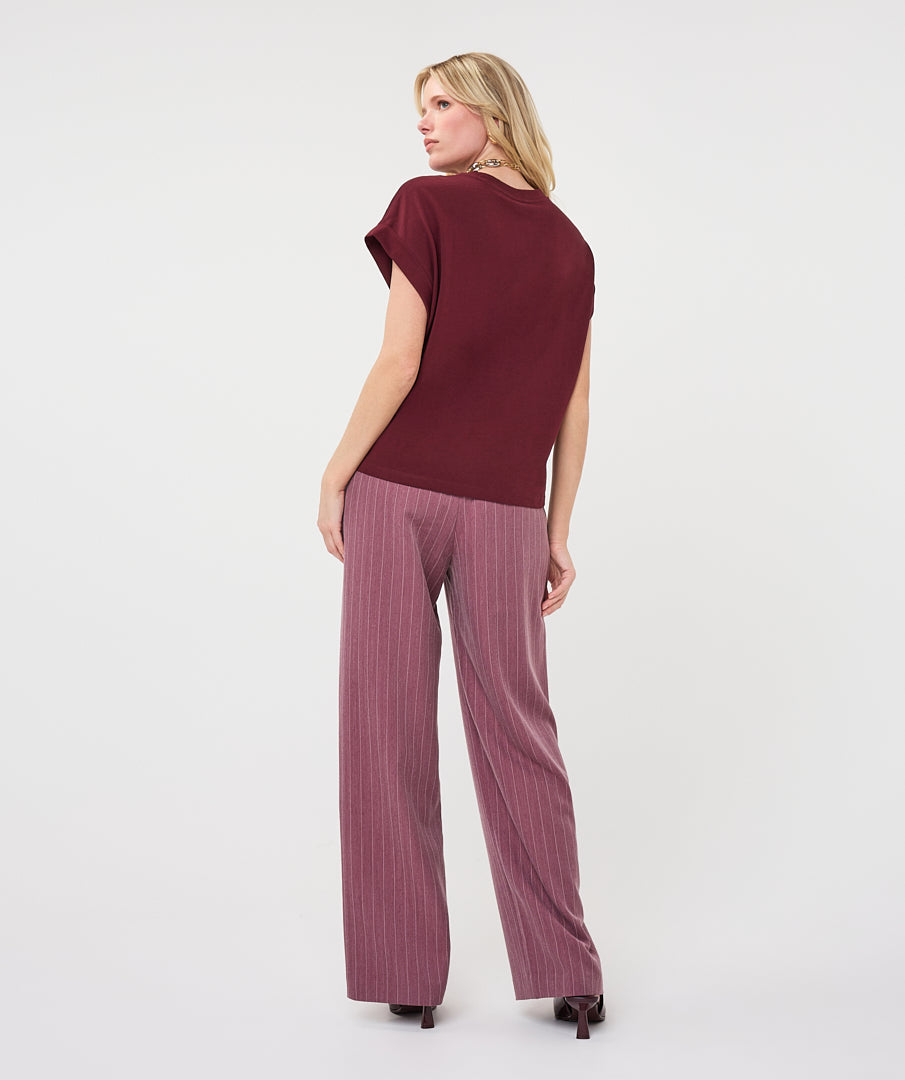 Woman wearing a burgundy satin roll-sleeve top with mauve pinstripe wide-leg trousers