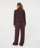 Model wearing a tailored wide-leg trouser suit, shown from the back with a cropped blazer and flowing trousers.
