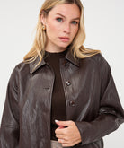 Woman wearing a dark brown cropped faux leather jacket with a collared neckline and button-front closure, styled with a brown knit top