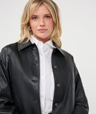 Woman wearing a dark gray cropped faux leather jacket with a collared neckline and button-front closure, layered over a white button-up shirt