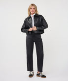  Woman wearing a dark gray cropped faux leather jacket with a collared neckline and button-front closure, layered over a white button-up shirt and paired with black straight-leg jeans and black-and-white sneakers.