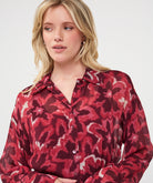 Woman wearing a burgundy and red abstract print button-front blouse with a collared neckline and long sleeves