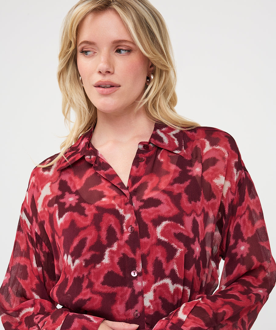 Woman wearing a burgundy and red abstract print button-front blouse with a collared neckline and long sleeves
