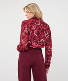 Back view of woman wearing a burgundy and red abstract print blouse with a relaxed fit and long sleeves, tucked into high-waisted burgundy pants.