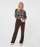 Full-length view of a woman wearing a brown and taupe plaid short blouse with a white collar, paired with wide-leg brown trousers and sneakers.