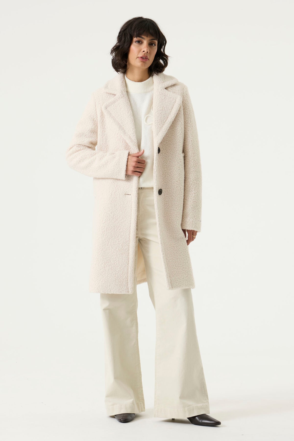 Woman wearing a cream Lennox Textured Coat with notched lapels, button front and side pockets.