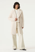 Woman wearing a cream Lennox Textured Coat with notched lapels, button front and side pockets.