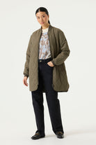 Woman modelling a longline olive green quilted jacket with a ribbed collar and cuffs, full front zip closure, side pockets, and rounded hem.
