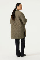 Woman modelling a longline olive green quilted jacket with a ribbed collar and cuffs, full front zip closure, side pockets, and rounded hem.