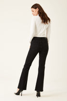 Woman wearing black flared jeans and a white turtleneck on a white background