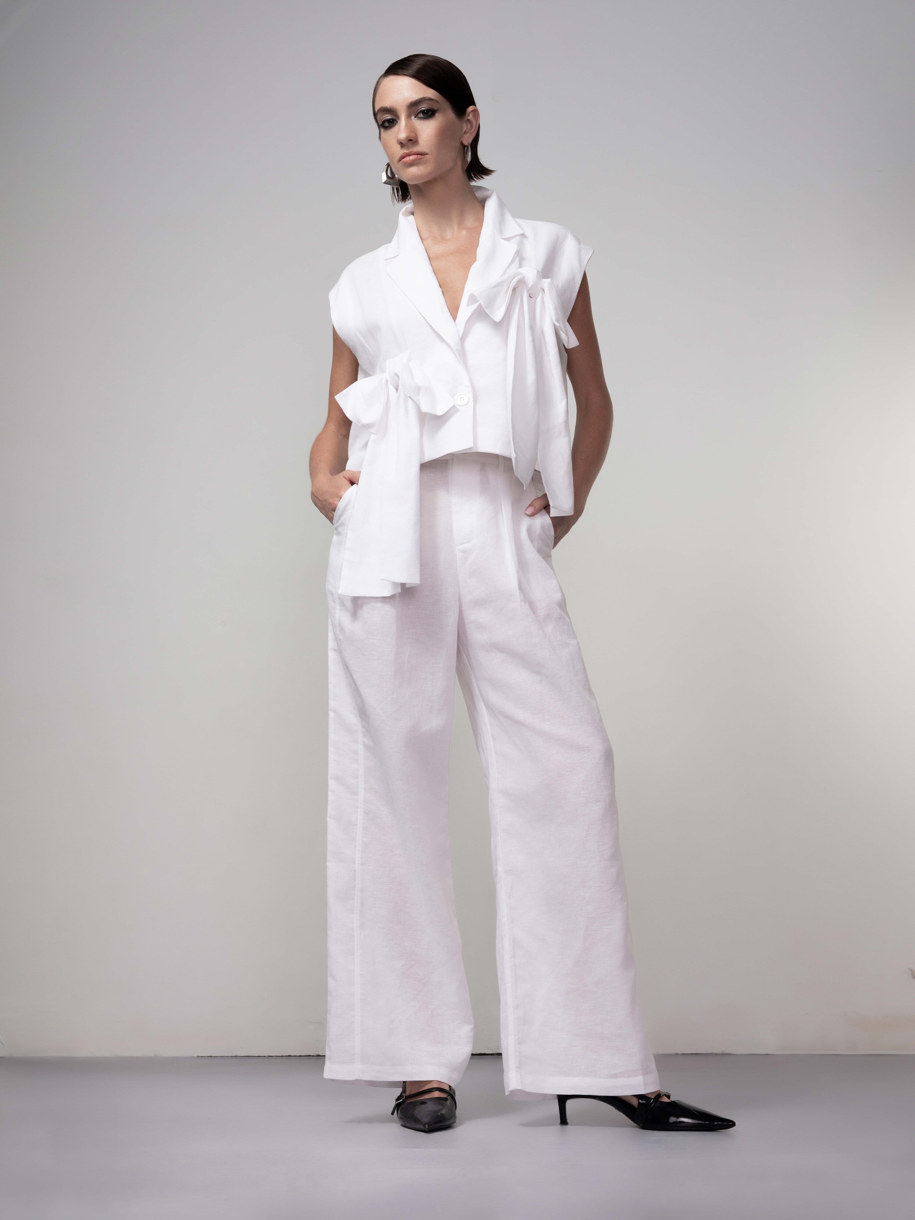 Model wearing relaxed wide-leg linen blend pants with a high-rise fit, styled with a sleeveless cropped top featuring soft draped details and pointed heels, standing against a neutral studio background.