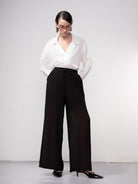 Woman wearing black wide-leg drawstring pants paired with a white blouse and pointed-toe heels, standing against a neutral background.