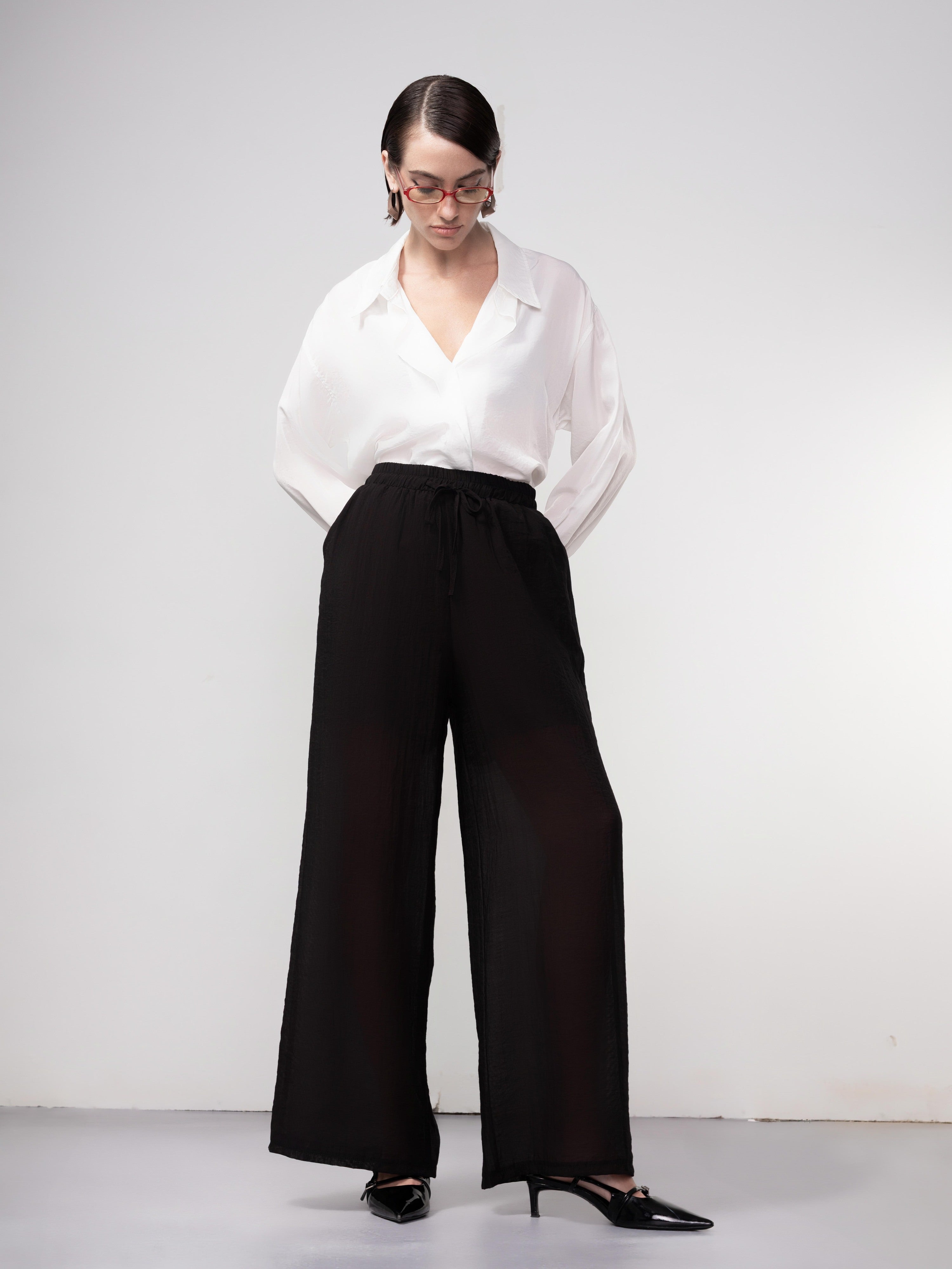 Woman wearing black wide-leg drawstring pants paired with a white blouse and pointed-toe heels, standing against a neutral background.
