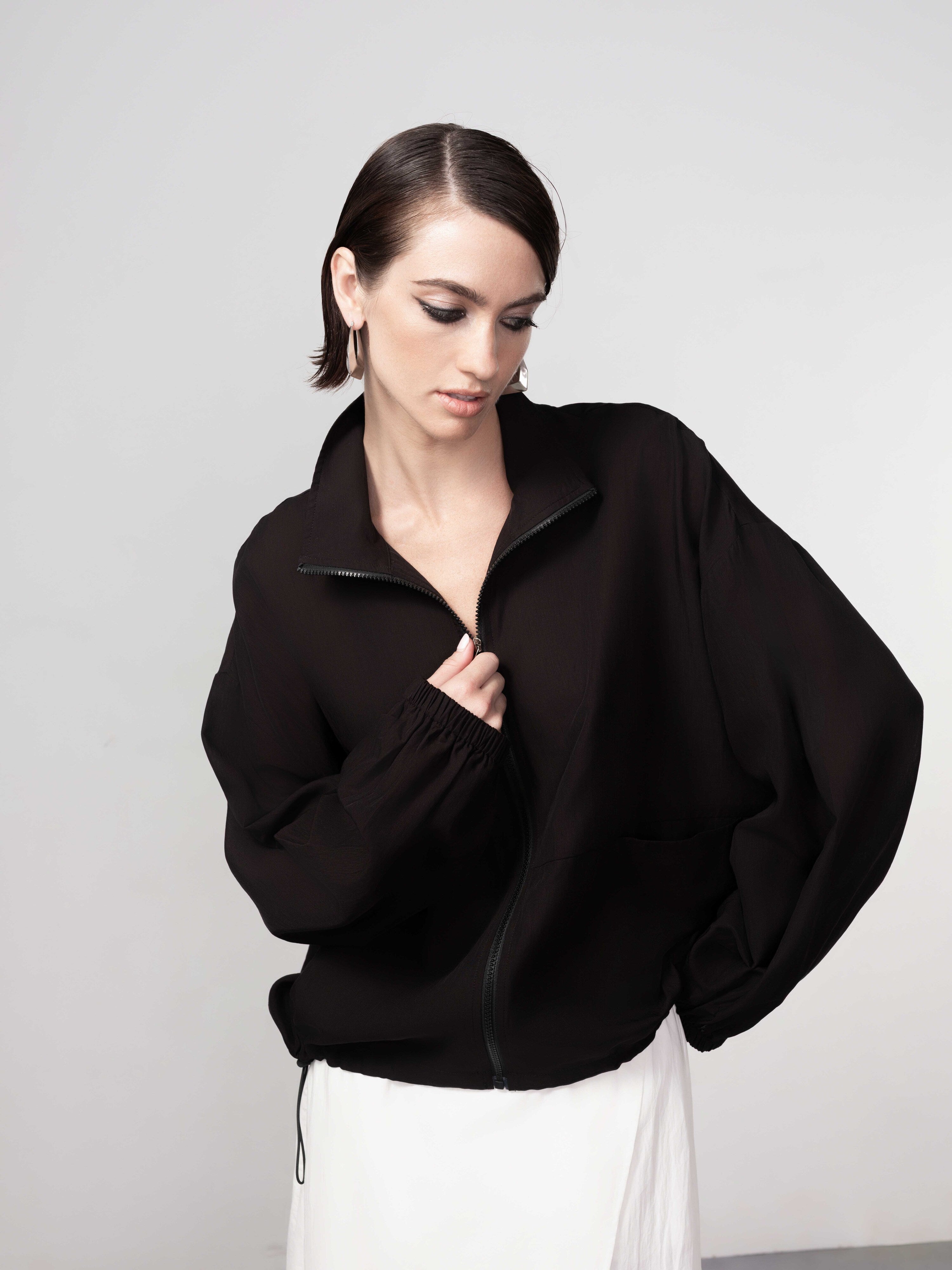Model wearing a black lightweight zip-front blouse with long sleeves and a white midi skirt