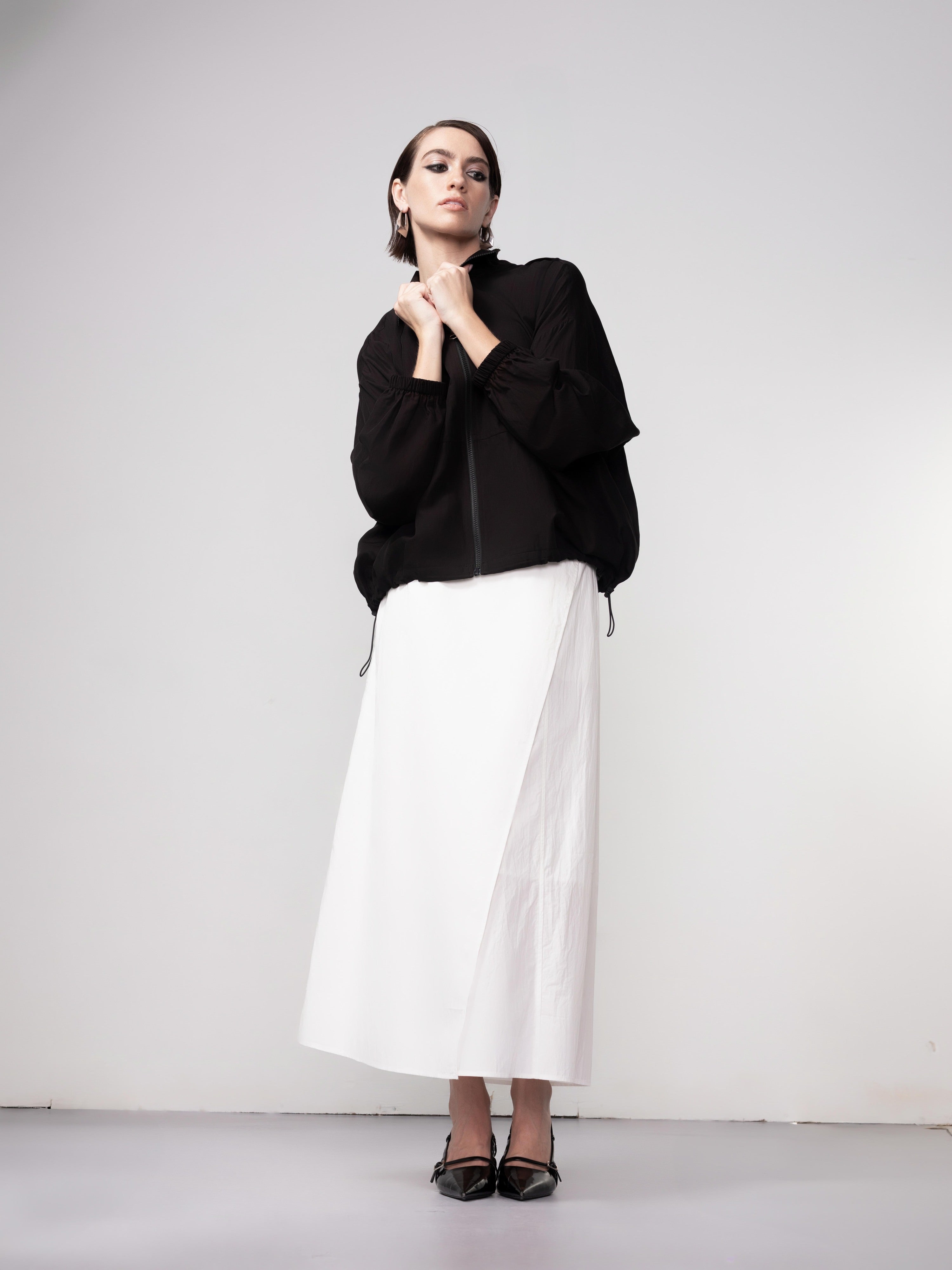 Model wearing a black lightweight zip-front blouse with long sleeves and a white midi skirt