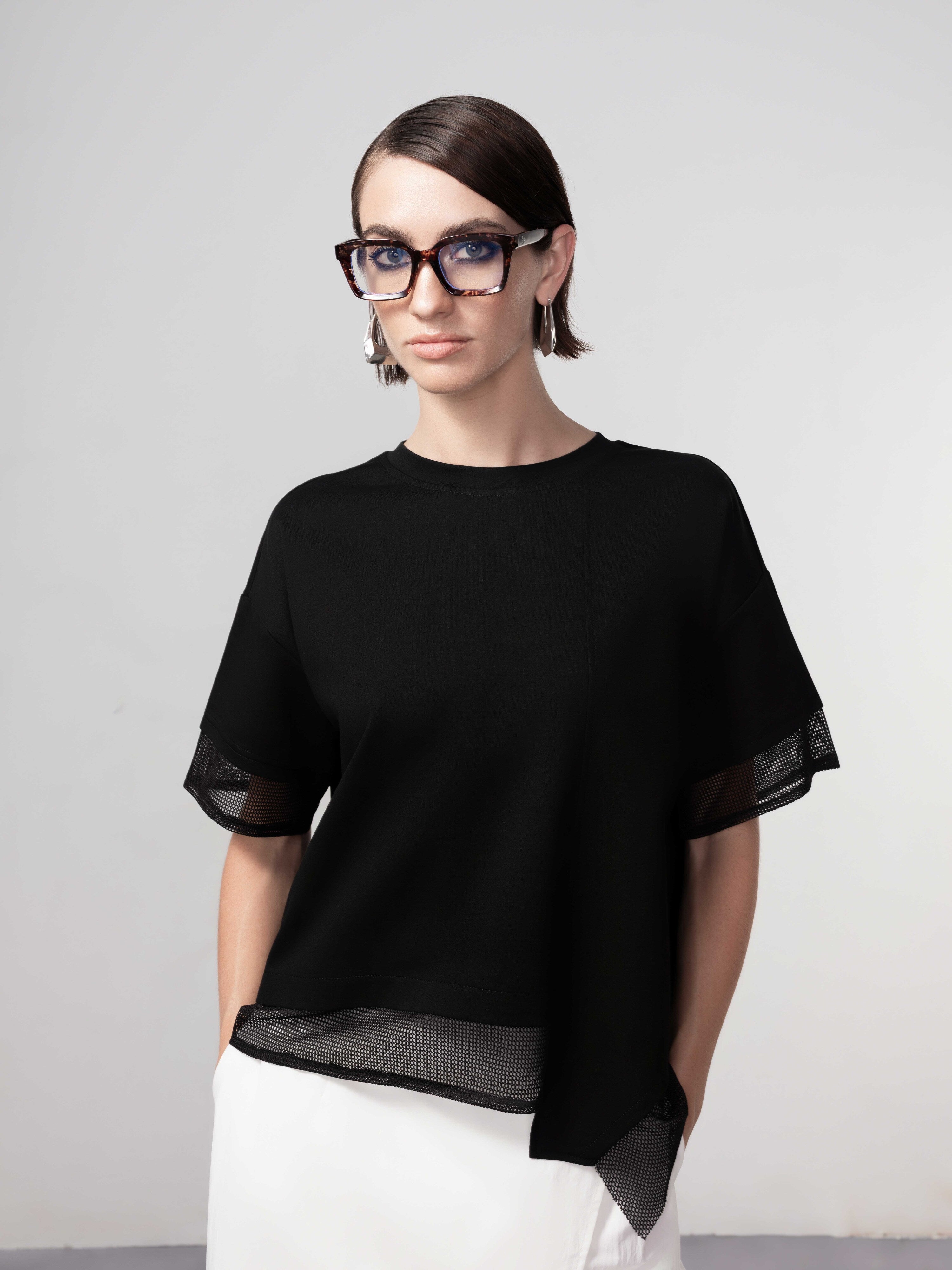 Close-up of a model wearing a black short-sleeve blouse featuring a soft drape and sheer mesh trim detailing along the sleeves and hem.