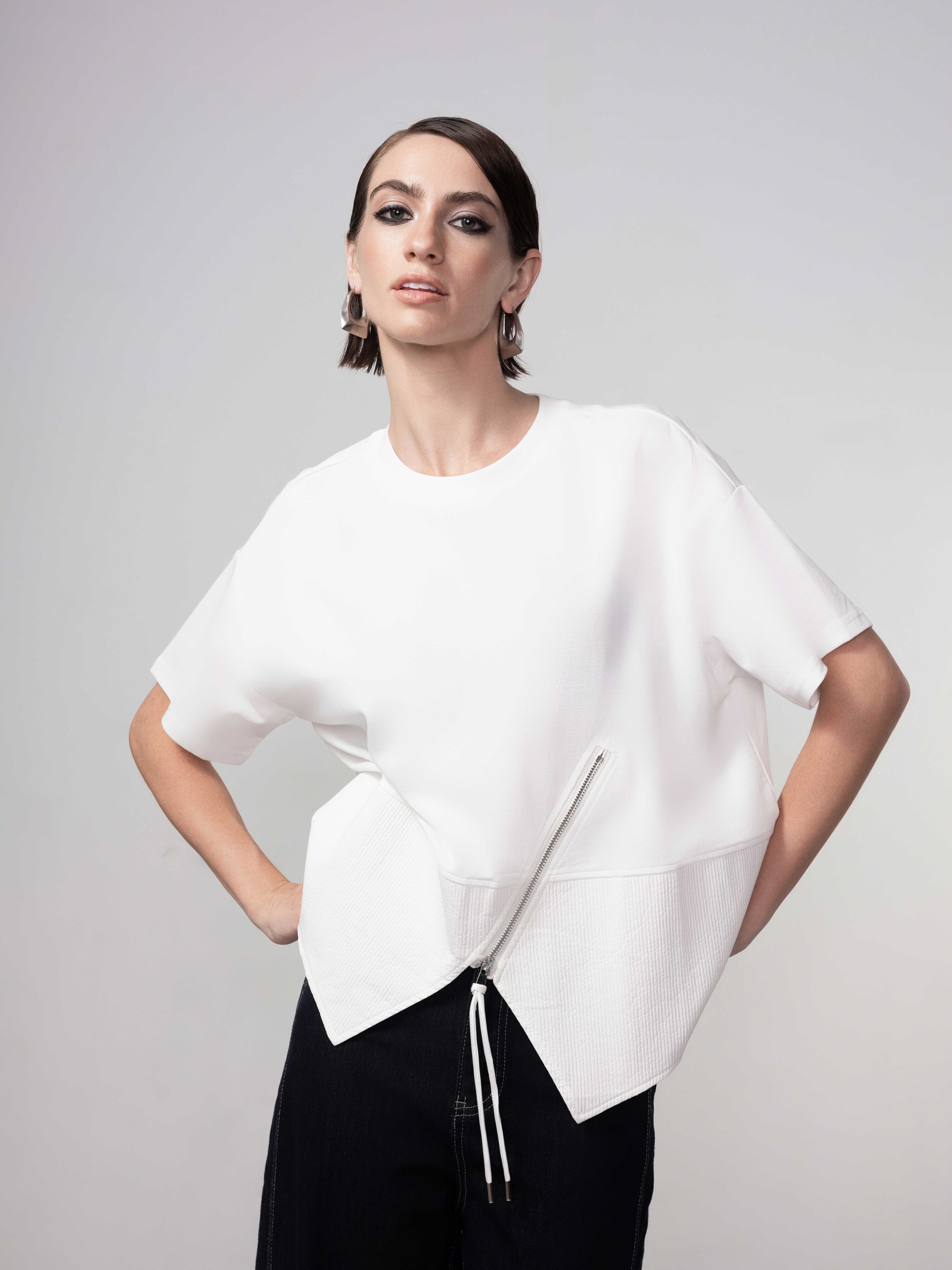 Model wearing a white asymmetrical zip pullover with short sleeves and relaxed fit, front view detail