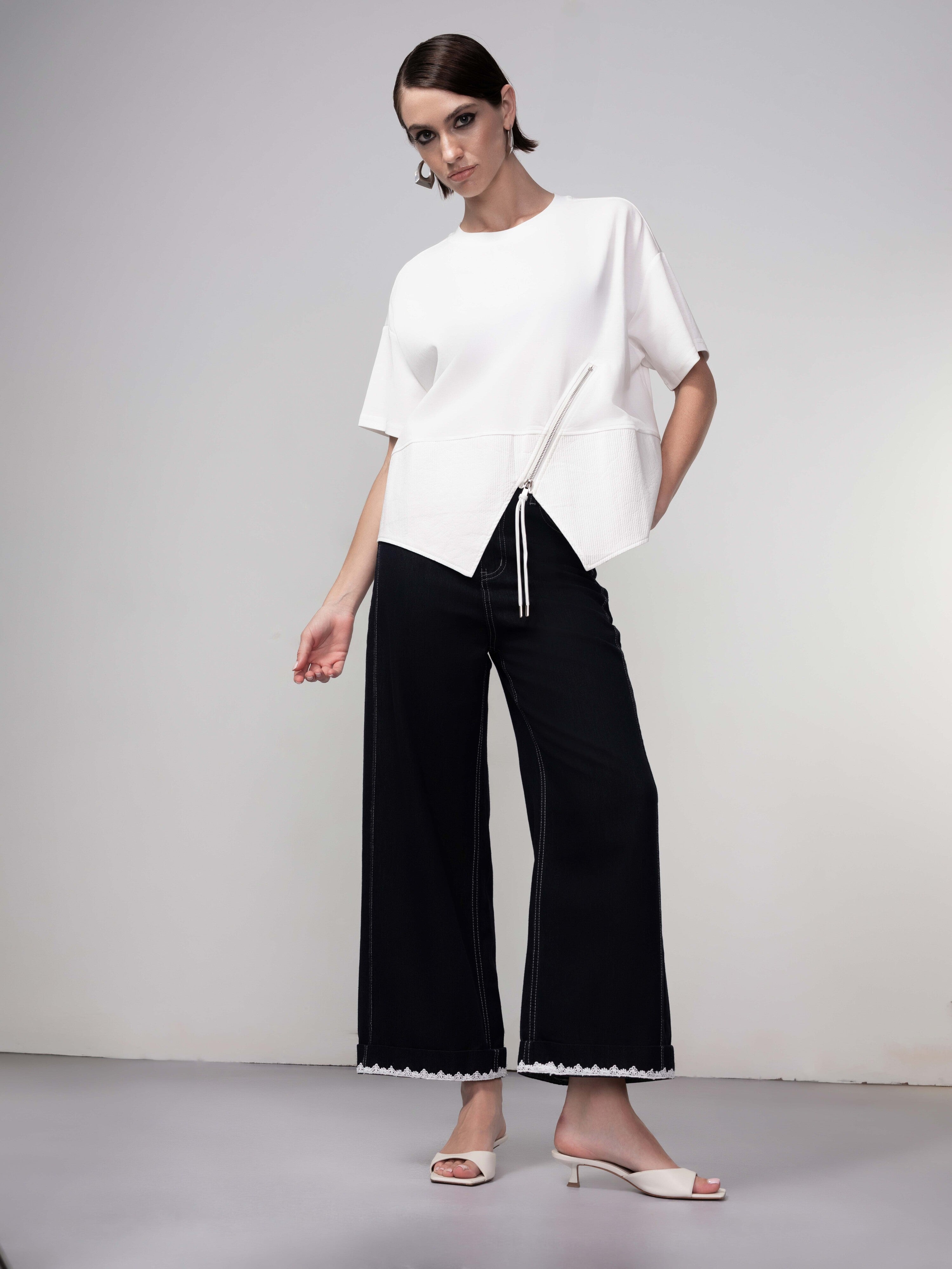 Full-length view of model in a white asymmetrical zip top paired with black wide-leg cropped pants and heeled sandals