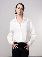 Woman wearing a crisp white cotton blouse with a relaxed fit, classic collar, and long sleeves, paired with dark high-waisted jeans, styled with a clean, modern look.