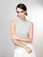 Model wearing a light grey sleeveless knit sweater with a fitted silhouette, featuring a smooth fine-gauge texture and clean crew neckline, paired with a soft white skirt, styled with minimal accessories against a neutral studio background.