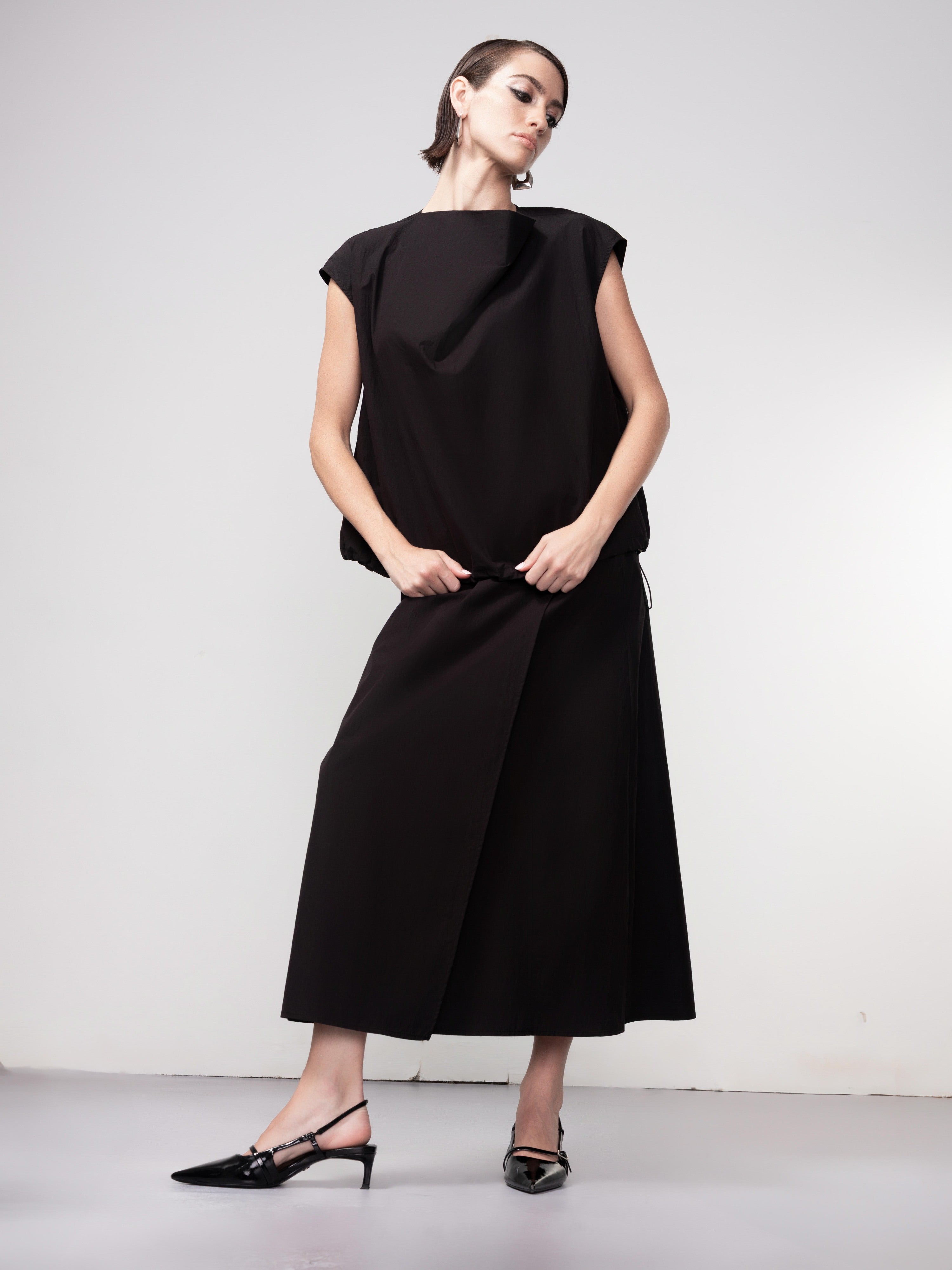 Woman wearing a black cocoon-style pullover top paired with a matching midi skirt and pointed slingback heels, shown in a full-length studio pose.
