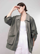 Model in a khaki green relaxed-fit jacket with rolled sleeves, styled over a white top and matching bottoms, posing against a soft grey backdrop.