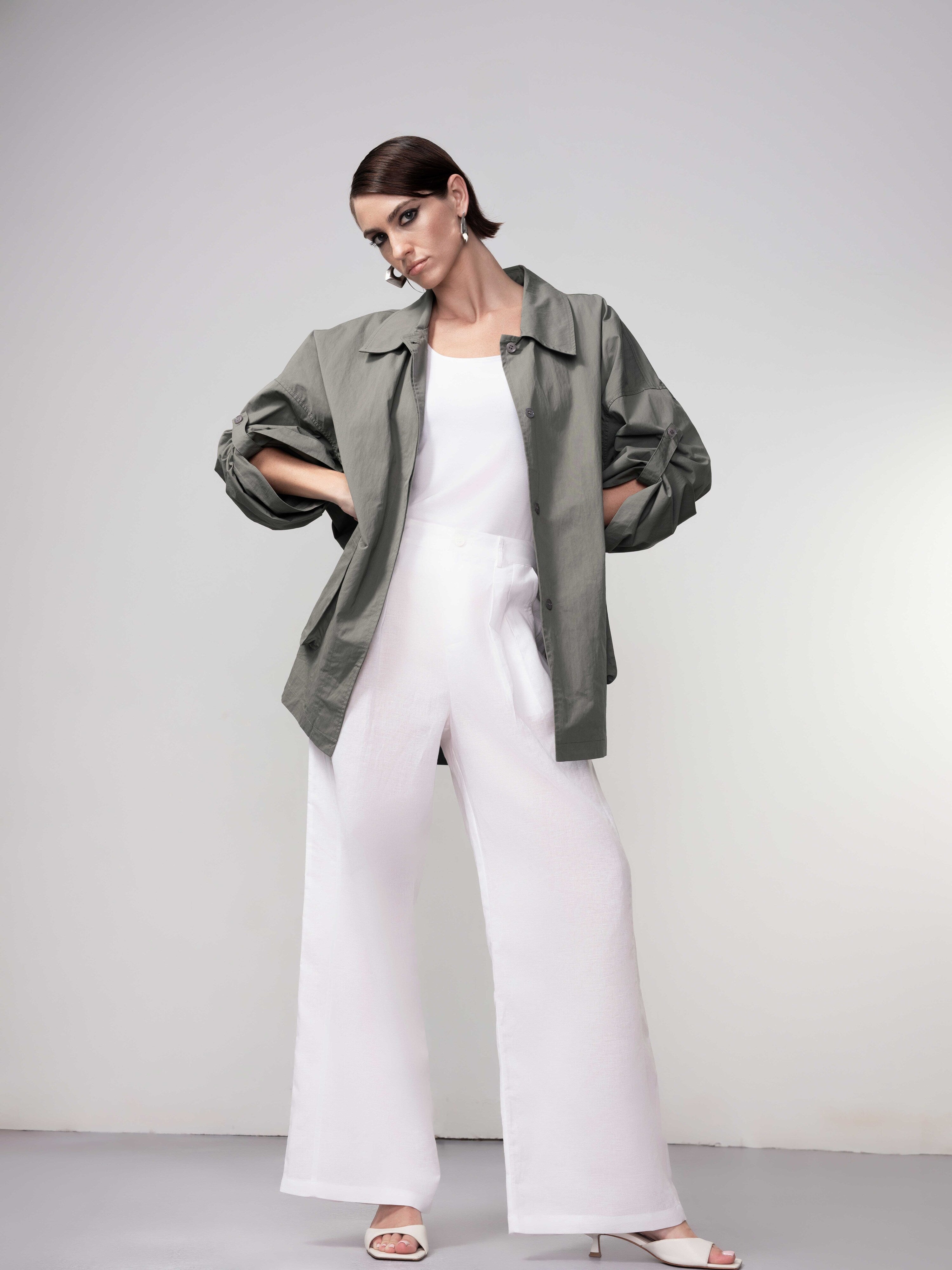 Model in a khaki green relaxed-fit jacket with rolled sleeves, styled over a white top and matching bottoms, posing against a soft grey backdrop.