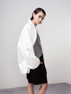 Model wearing a white lightweight jacket layered over a black and white striped top, styled with dark bottoms in a studio setting.