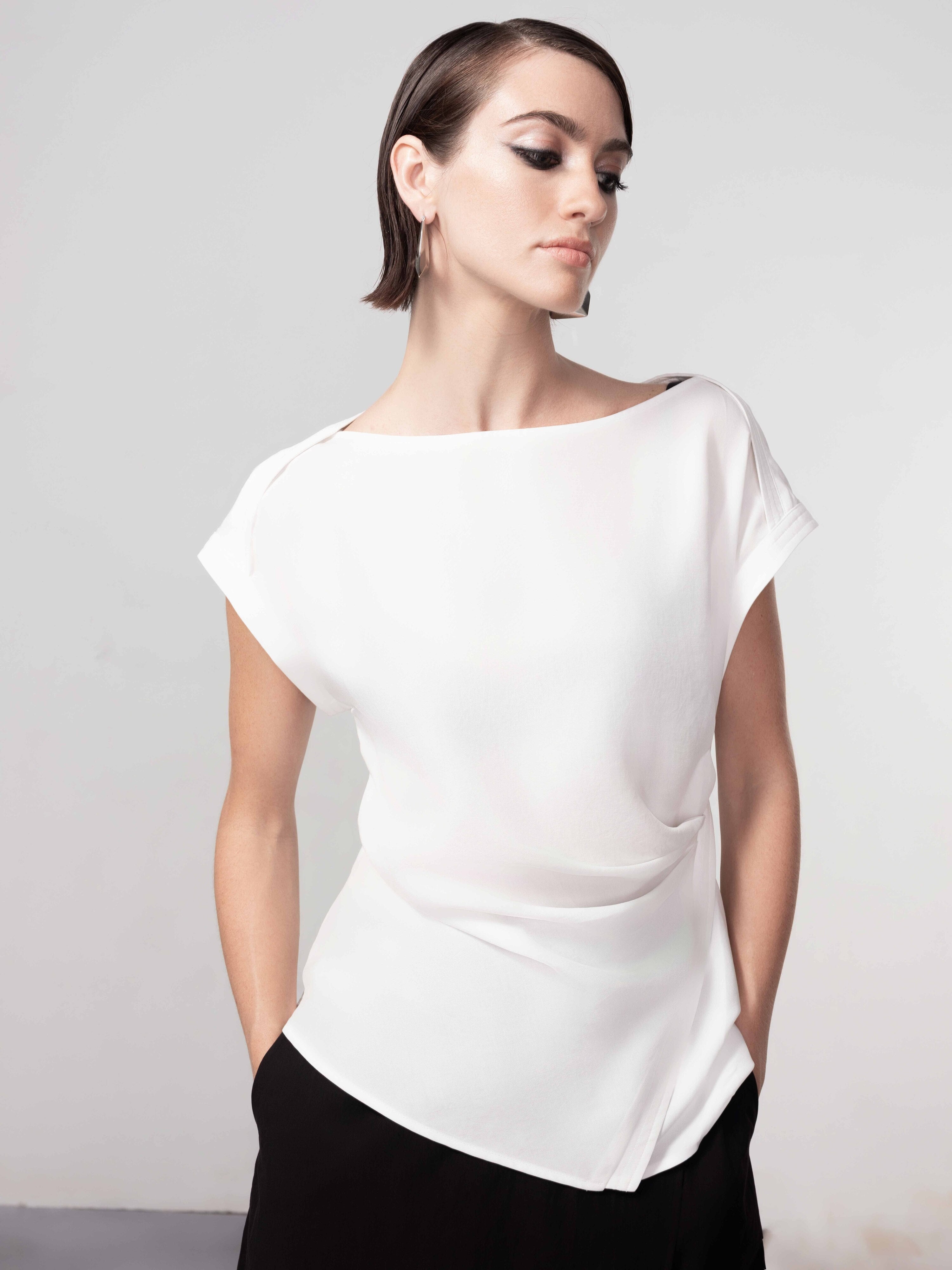 Woman wearing a white short sleeve draped blouse with an asymmetrical hem, styled with a black midi skirt