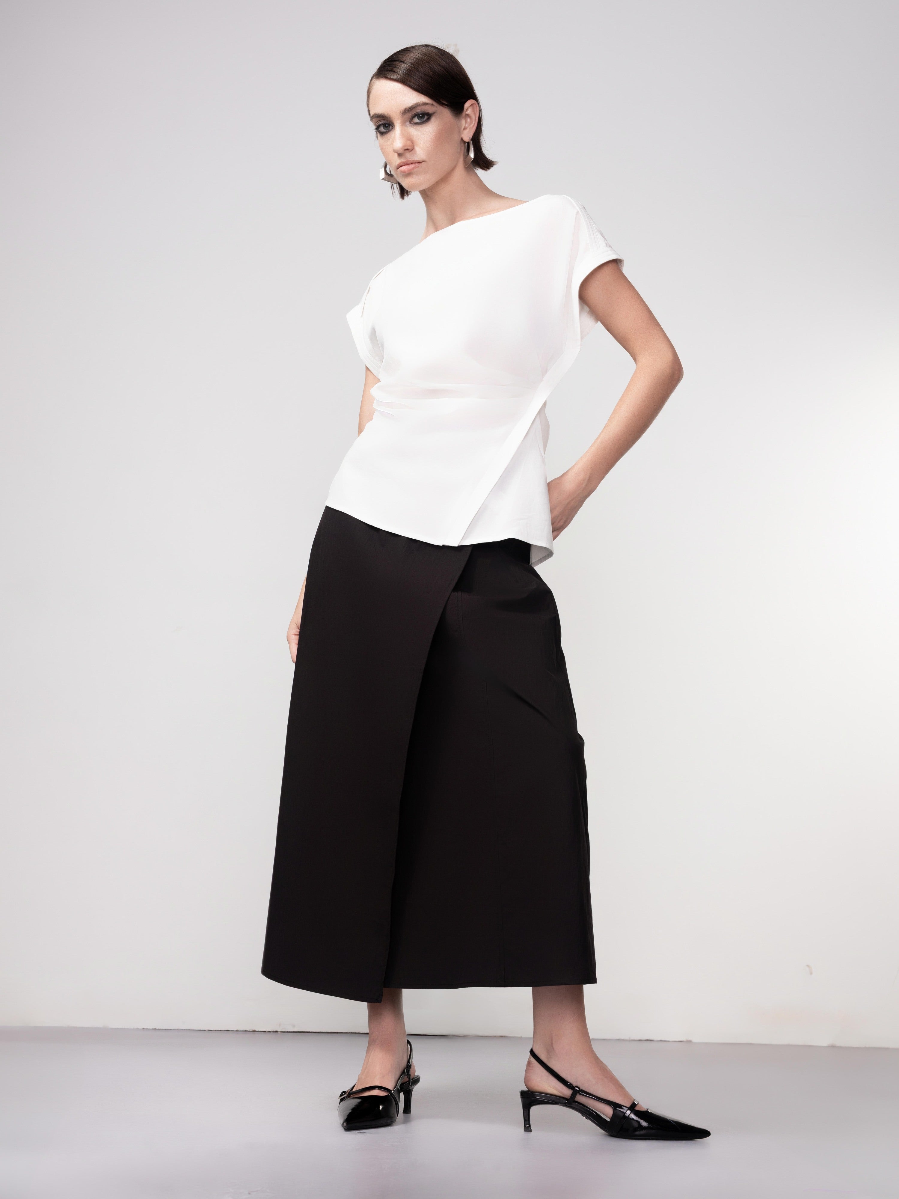 Woman wearing a white short sleeve draped blouse with an asymmetrical hem, styled with a black midi skirt