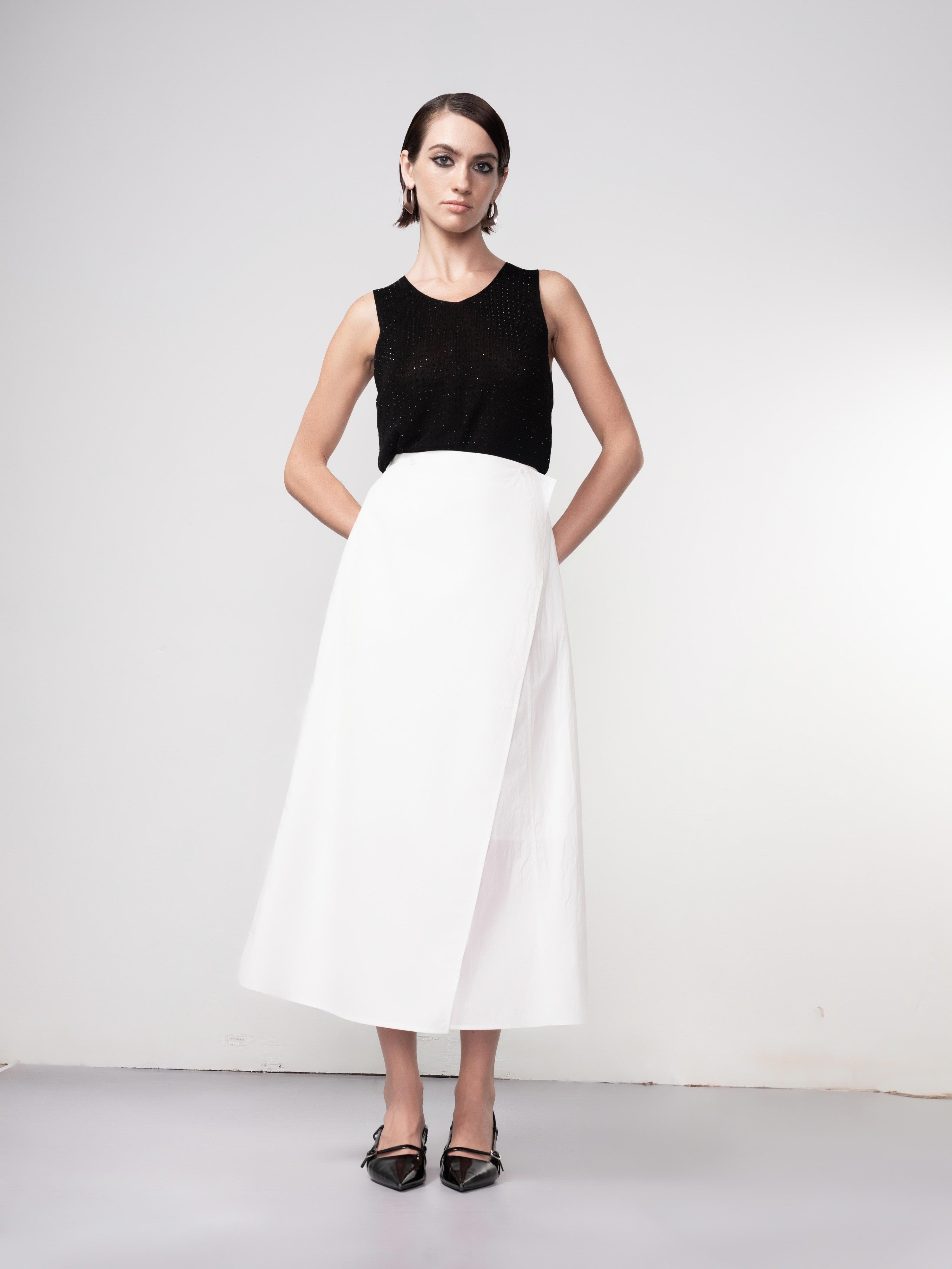 Model wearing a white short-sleeve blouse paired with a black midi A-line wrap skirt and pointed slingback heels, angled view.