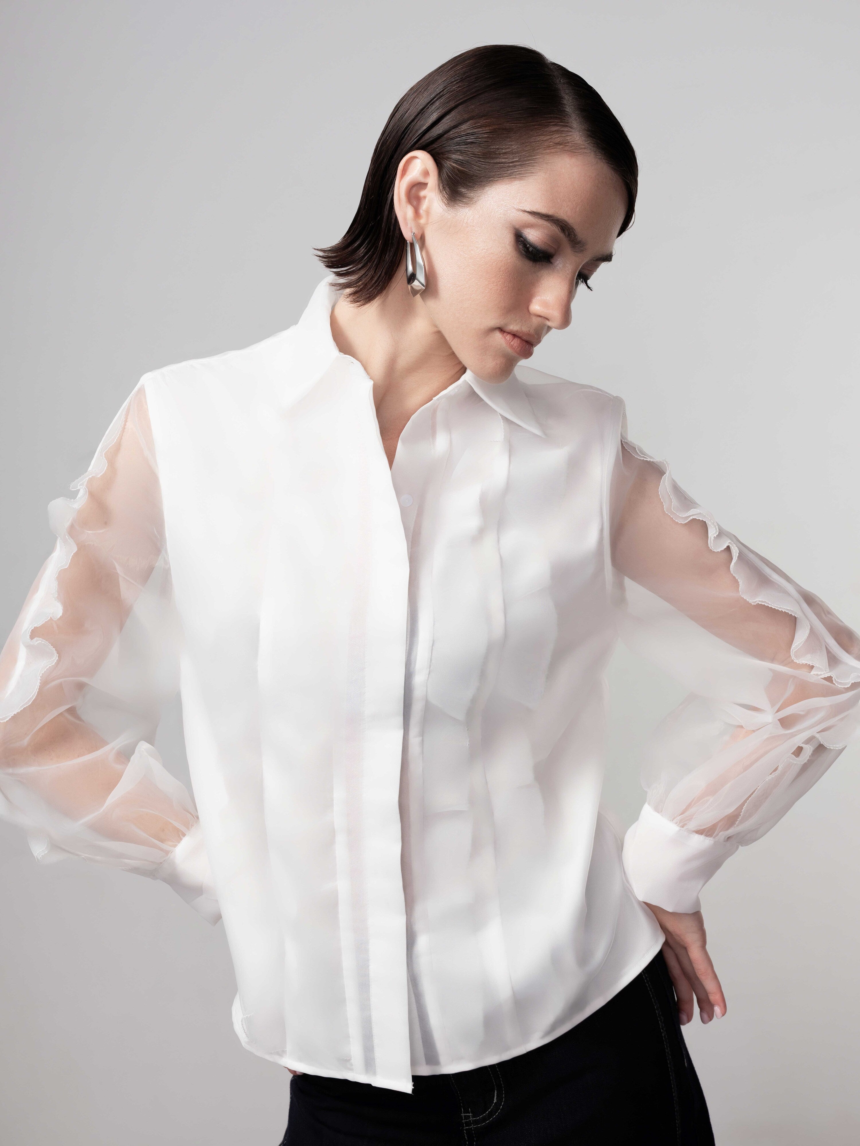 Close-up of a white layered blouse with sheer long sleeves, soft ruffle detailing, and a clean front design on a model