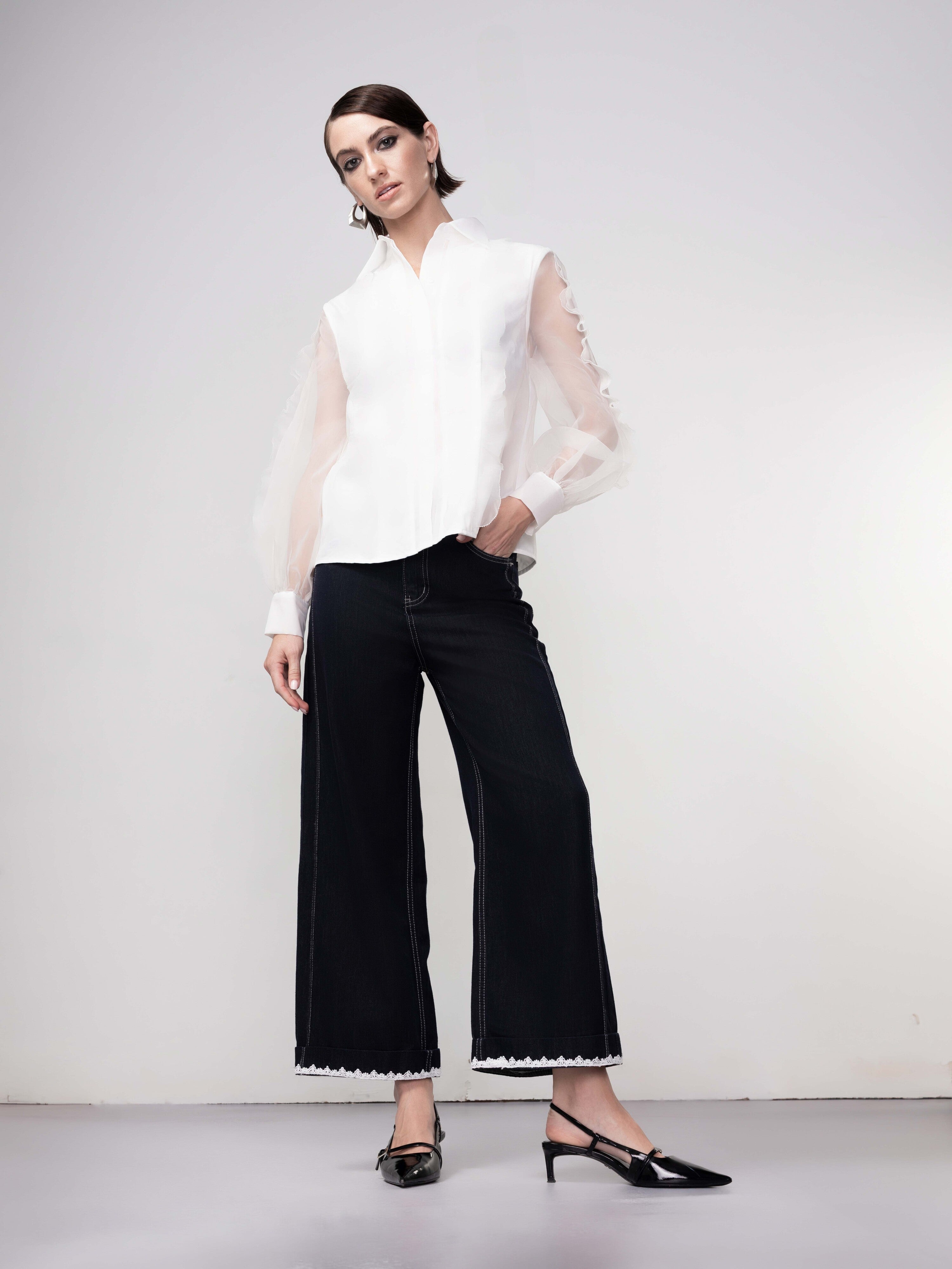 Full-length view of a model wearing a white sheer sleeve layered blouse with wide-leg dark denim jeans and black slingback heels