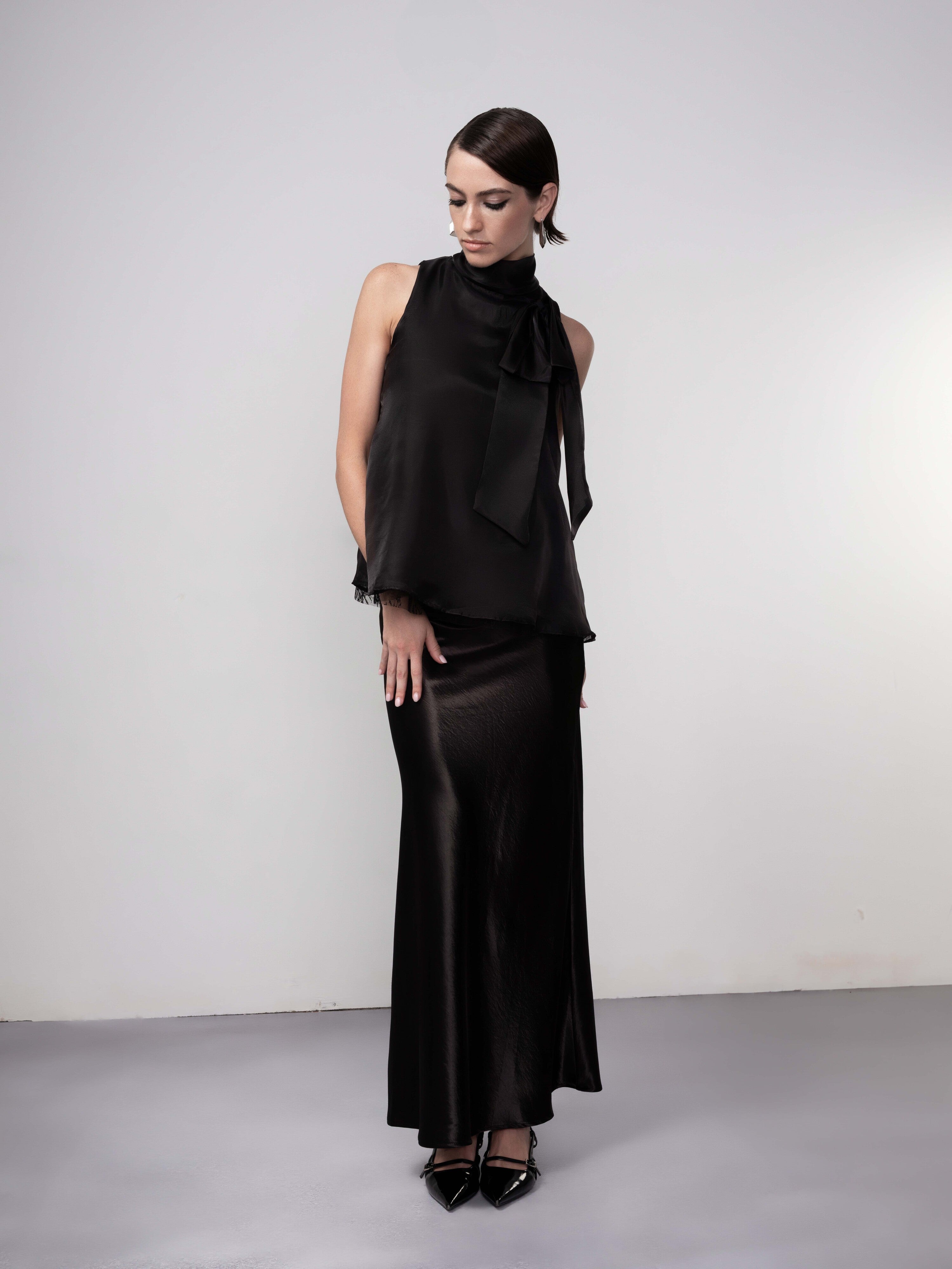 Full-length view of a black sleeveless satin blouse paired with a matching long skirt, styled in an elegant, minimal look.