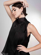 Woman modelling a black sleeveless satin blouse with tie-neck detail, shown in a close-up side pose with arm raised.