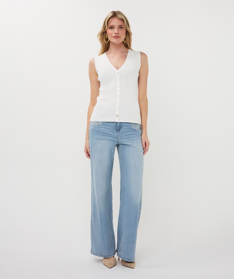 Model wearing light wash embroidered wide-leg jeans styled with a sleeveless knit top and heels, showcasing a relaxed yet polished outfit.
