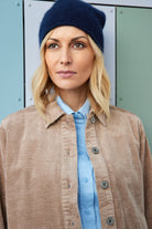 Woman wearing a navy beanie and beige corduroy jacket against a metallic wall.