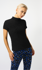 blonde woman wearing black textured top and blue patterned pants