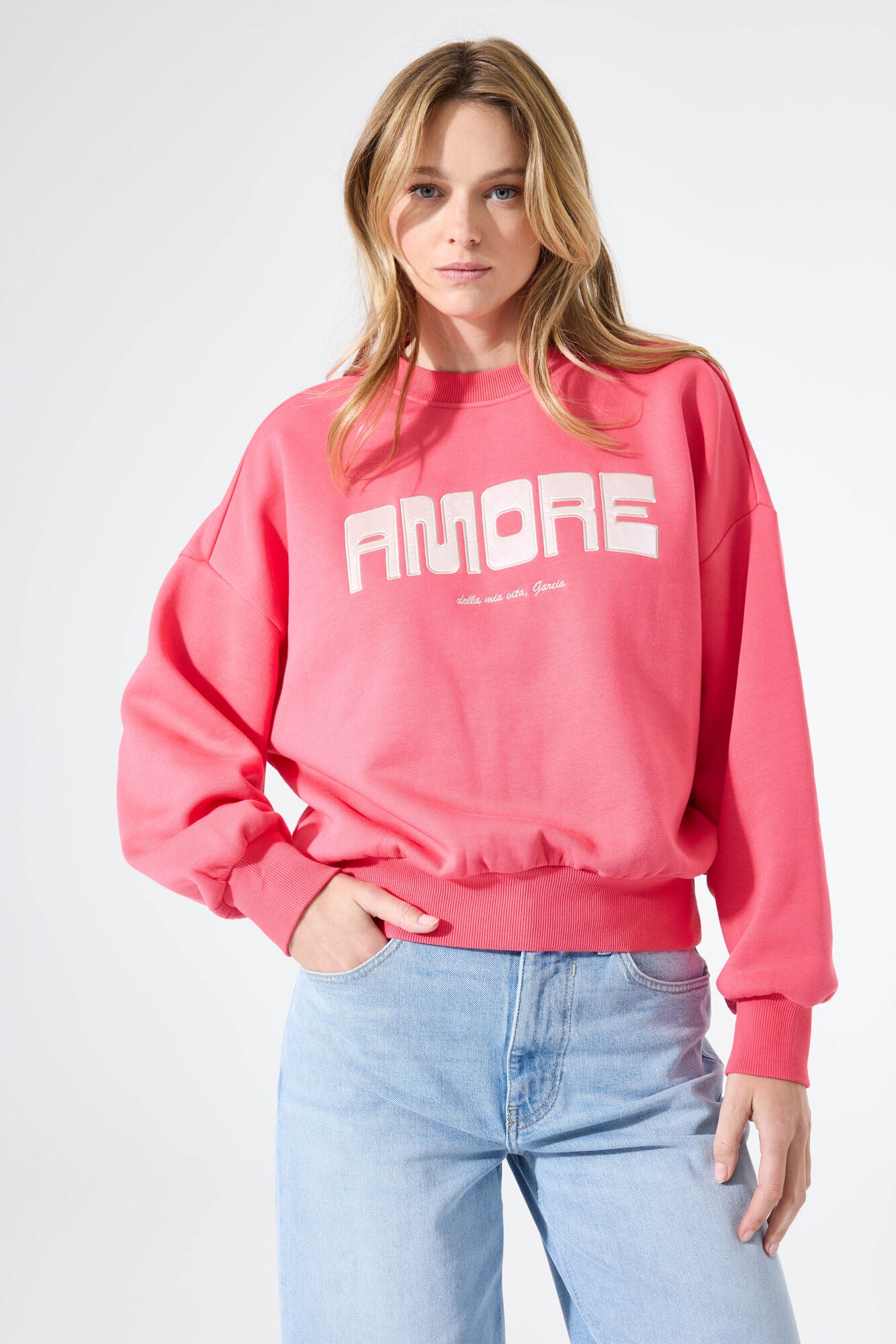 Woman wearing a relaxed crewneck sweatshirt with a bold “Amore” graphic on the front, styled with wide-leg jeans