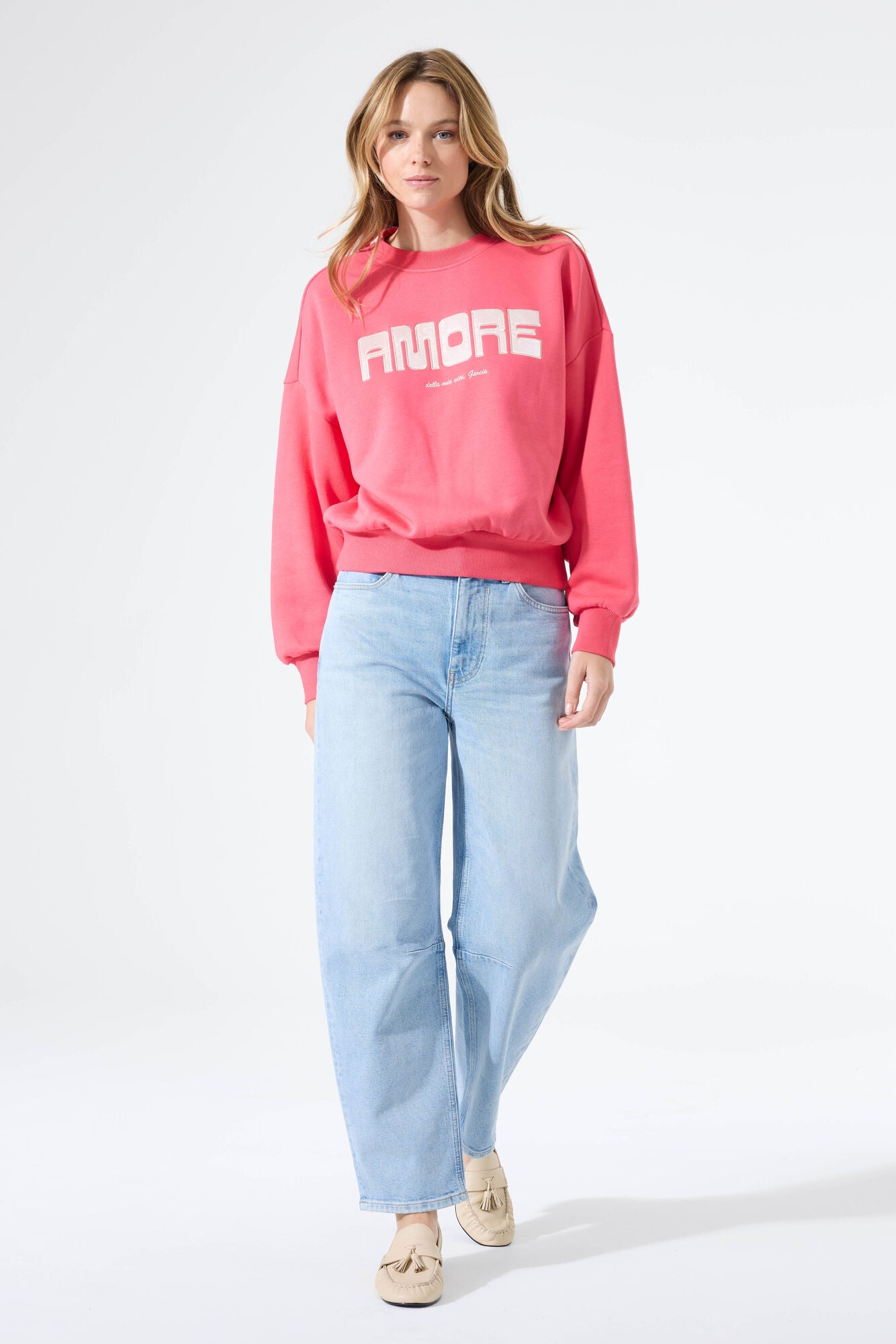 Woman wearing a relaxed crewneck sweatshirt with a bold “Amore” graphic on the front, styled with wide-leg jeans and loafers, walking forward.