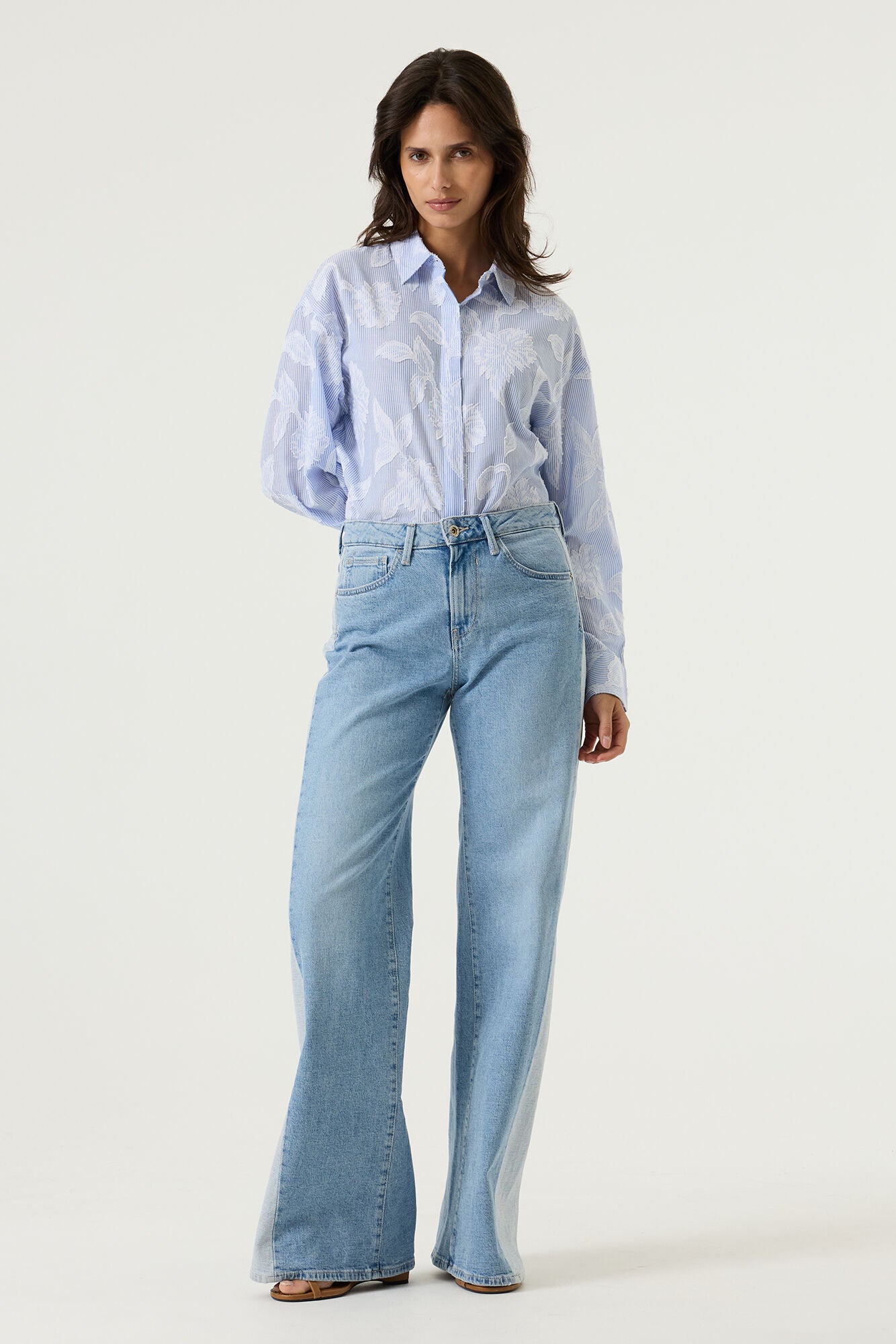 Women's light blue striped cotton blouse with textured floral detailing, featuring a collared neckline, button-front design, and relaxed fit. Tucked into light wash wide-leg jeans for an effortless everyday look.